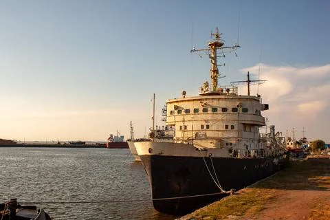 Large white and black cargo ship docked at harbor. Sunset casts warm glow ove Stock Photos