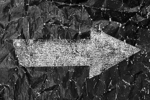 A large white arrow points right on crumpled black paper, emphasizing contras Foto stock