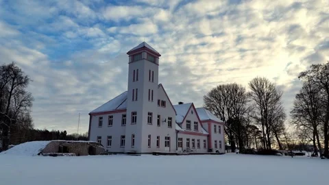 A large white building with a clock tower stands alone in a snowy field, Stock Footage 269948301