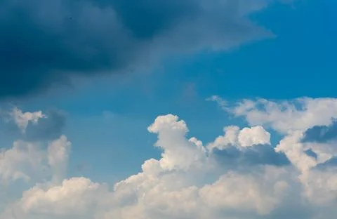 Large white cloud behind rain cloud on clear blue sky background. Photos