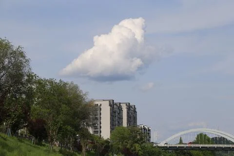 Large white cloud over riverside apartments and arched bridge in a green ur.. Stock Photos