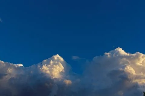 Large white clouds in a blue sky with the moon. Stock Photos