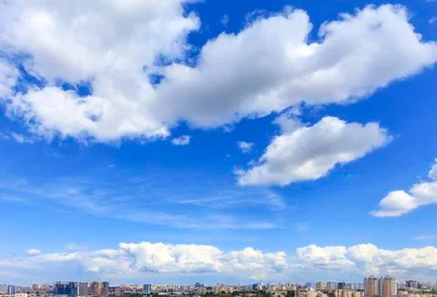Large white clouds float in the blue sky above the city skyline. Stock Photos