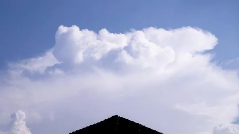 Large White Cumulus Cloud Above Residential Rooftop And Blue Sky Stock-Fotos