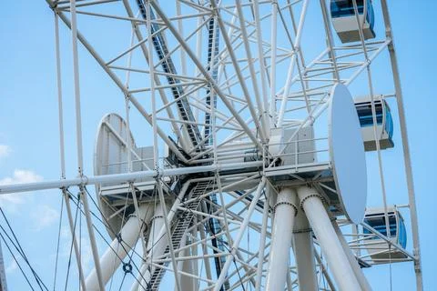 Large white Ferris wheel structure with blue passenger cabins against a cle.. Foto stock