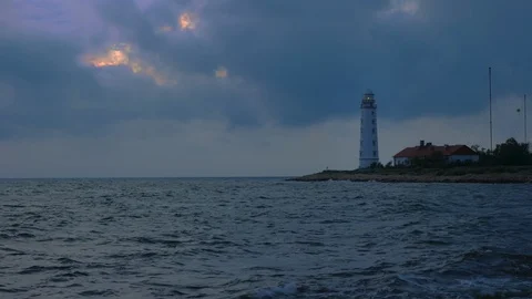 A large white lighthouse on the seashore shines yellow light. Stock-Footage 111892687