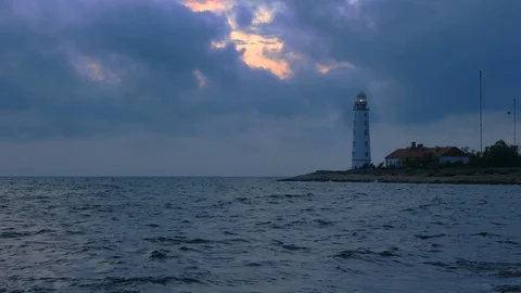 A large white lighthouse on the seashore shines yellow light. Video stock 111896536