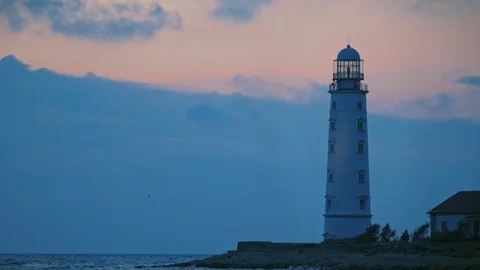 A large white lighthouse on the seashore shines yellow light. Video stock 111898568