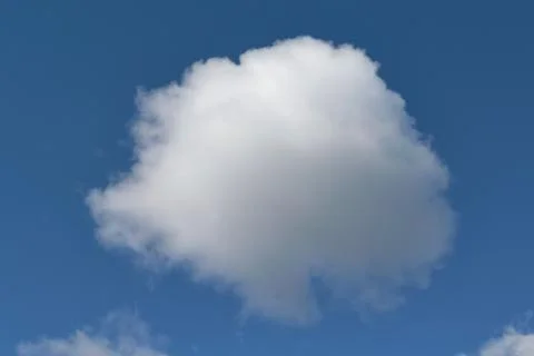 A large white lumpy cloud in the shape of a ball in a clear blue sky. Stock Photos