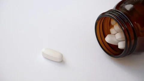 A large white oval tablet drops out of a brown glass bottle. Video stock 108688980