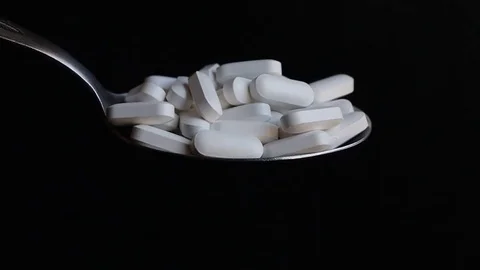 Large white pills being poured out of a spoon Stock Footage 125759403