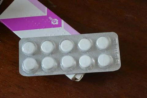 Large white pills in silver packaging arranged on a brown wooden background. Stock Photos