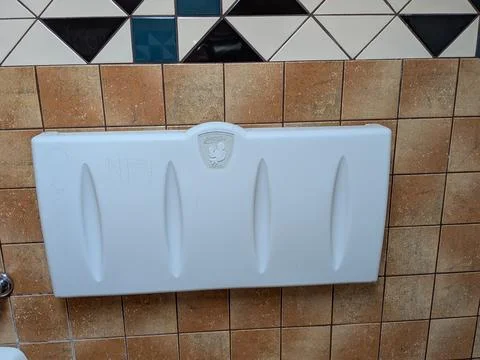 Large white plastic baby changing station mounted on a tile wall Stock-Fotos