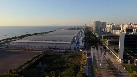 Large white-roofed venue by oceanfront with modern buildings; Parque das Nacoes Видео 346119116