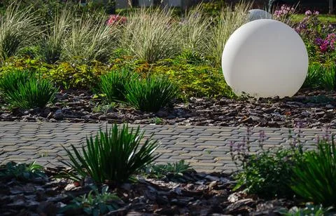 Large white round lamp standing on bark mulch bed in beautifully landscaped Stock Photos
