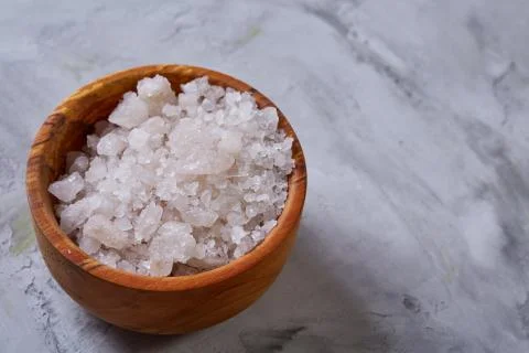 Large white sea salt in a natural wooden bowl on white background, top view Stock Photos