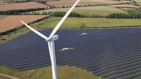 Large White Wind Turbine Rotating Above Solar Panel Fields on a Sunny Summer Stock Footage 340919164