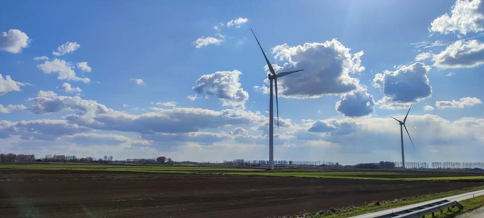 Large windmills stand in green fields against a blue sky Stock-Fotos