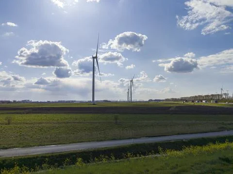 Large windmills stand in green fields against a blue sky Stock Photos