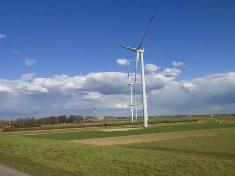 Large windmills stand in green fields against a blue sky Stockfoto's