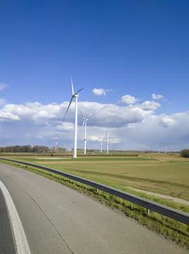 Large windmills stand in green fields against the blue sky by the road Stock Photos