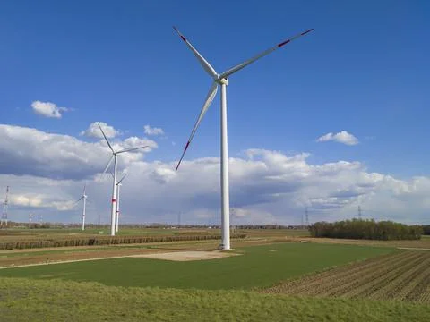 Large windmills stand in green fields against a blue sky Stock Photos