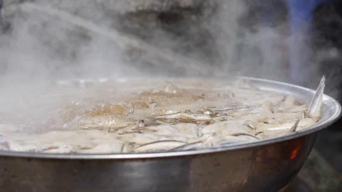 Large wok filled with boiling liquid where anchovies and salt simmer together Vidéo 333632682