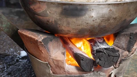 Large wok heating over open flame on a clay charcoal stove where fire and hot Stock-Footage 330724750