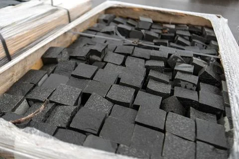Large wooden crate holds an array of square granite cobblestones, each uniq.. Stock Photos