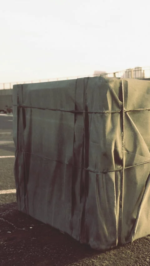 Large wrapped object sits on asphalt in an open area during daytime Stock Footage 336581778