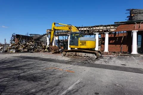 A large yellow backhoe in front of a building being demolished Stock Photos