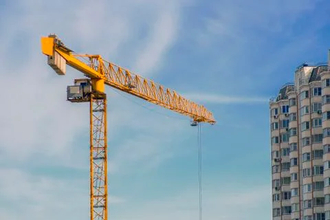 Large yellow construction crane, multi-storey house against the blue sky Stock Photos