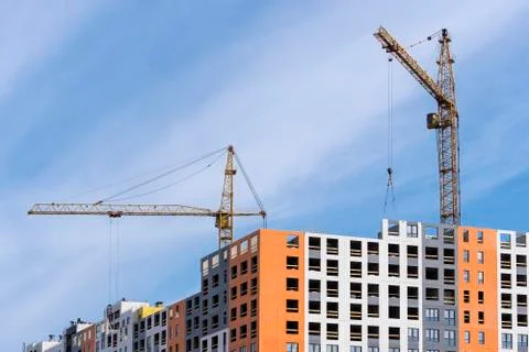 Large yellow construction crane, multi-storey house against the blue sky Stock Photos