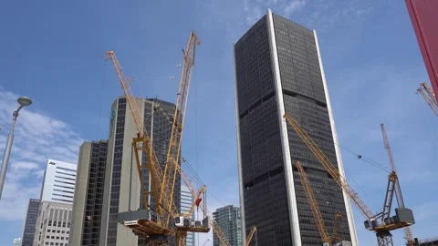 Large yellow construction cranes stand before tall corporate skyscrapers and Stock Footage 335306387
