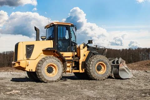 A large yellow front-loader sits idle on a construction site, surrounded by r Photos