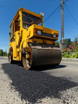A large yellow road roller on the side of a road Stock Photos