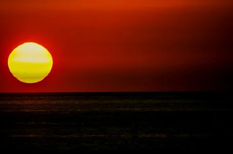 A large yellow sun is setting over the ocean Stock Photos