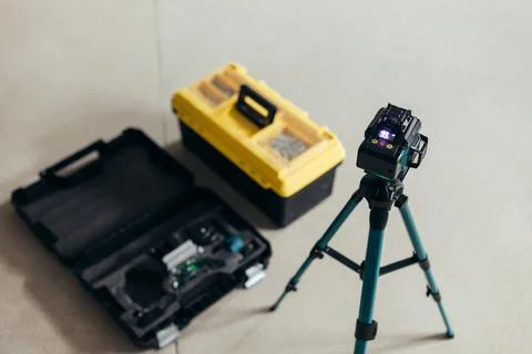 Laser Level Mounted On Tripod Next To Tool Cases. Professional Construction Stock Photos