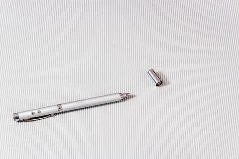 Laser pointer in the form of a telescopic stationery pen on a light backgroun Stock Photos