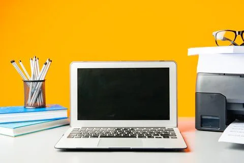 Laser printer and laptop on desk against yellow background Foto stock