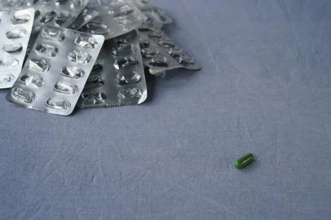 The last pill. A single green capsule and a pile of empty blister packs. Stock Photos