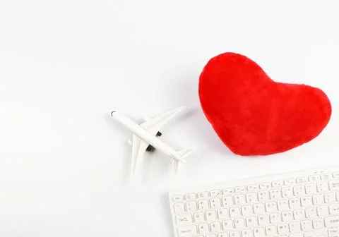 Lat lay of computer keyboard, heart shape pillow and airplane on white back.. Stock Photos