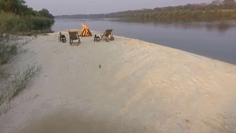 Late afternoon aerial view of sandy banks of Zambezi river, chairs, fire Stock Footage