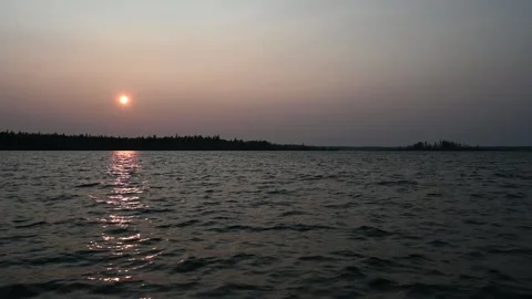 Late day orange sun setting into a smoky haze above a lake with small waves. Stock Footage 289479251