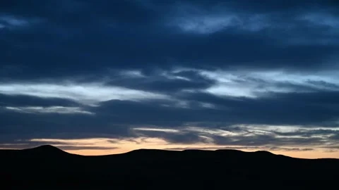 Late day time lapse of blue to dark gray clouds moving above rolling hills Stock Footage 285552581