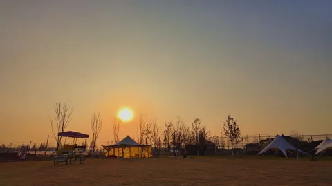 Late Golden Hour Sunset Over Dry Grass Glamping Field With Tents and Surrey Bike Stock Footage 334872151