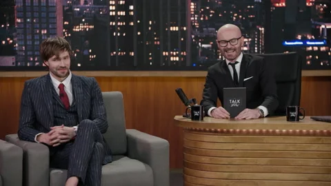 Late-night talk show host showing a green board to celebrity guest in a studio Stock Footage 147625316
