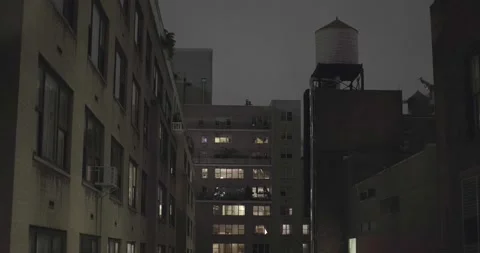 Late night upper floor window view out to building roofs with water tank. 4K Stock Footage 162592555