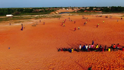 Lateral tracking shot of young people playing football on dirt field, Senegal Stock Footage 331991949