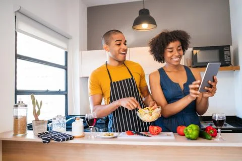 Latin couple using a digital tablet while cooking in kitchen. Stock Photos